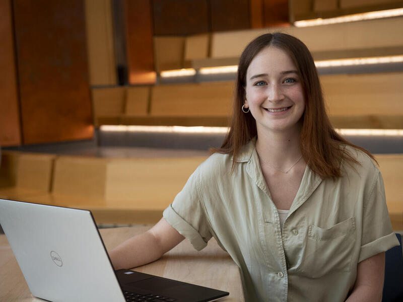 A woman sitting in a lecture room with a laptop in front of her 