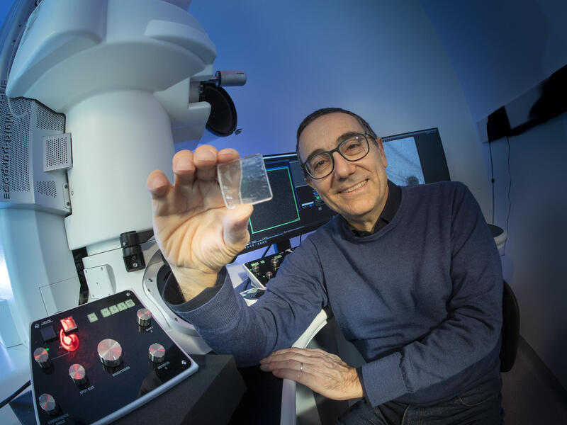 A photo of a man sitting from the waist up. He is holding a small piece of glass 