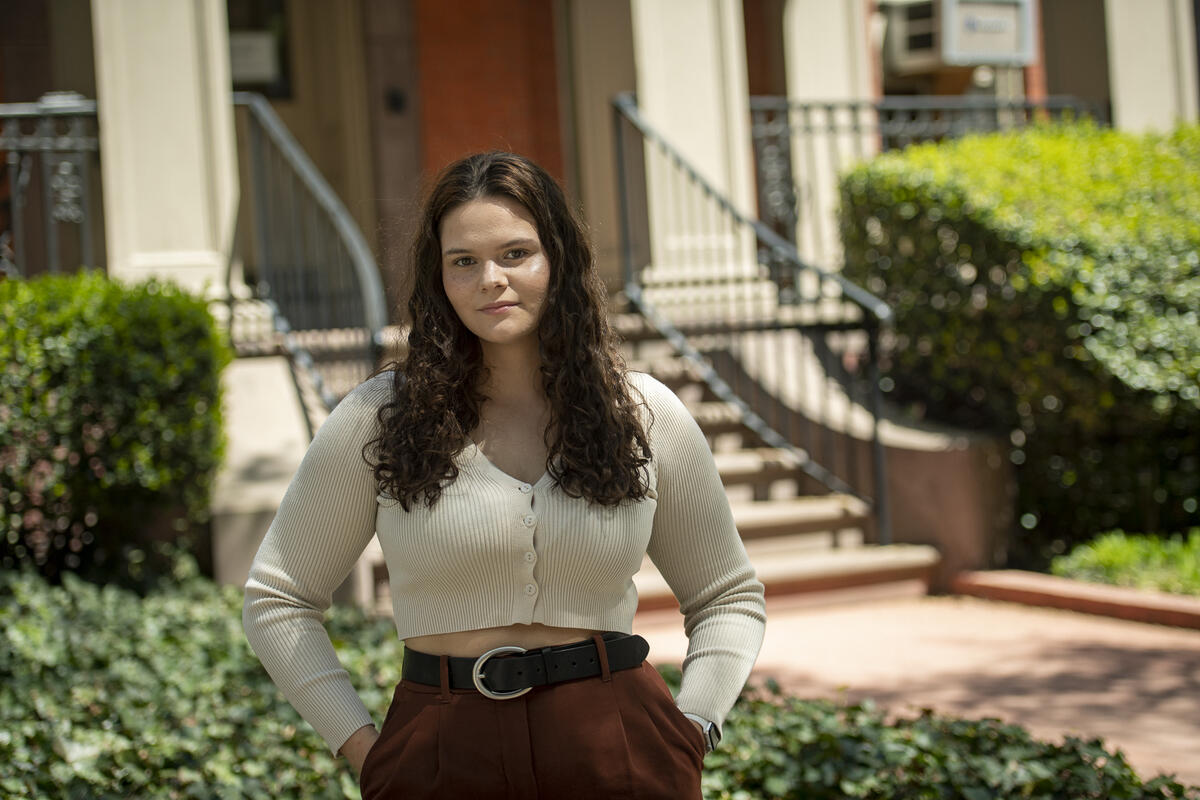 A photo of a woman standing outside with her hands in her pockets. 