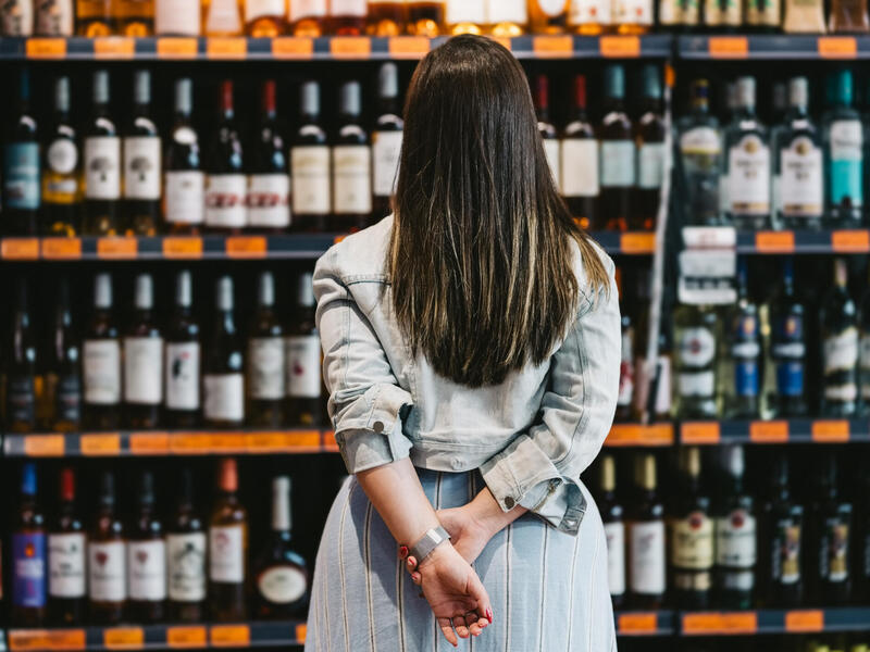 A photo of a woman standing in front of store shelves covered in wine. 