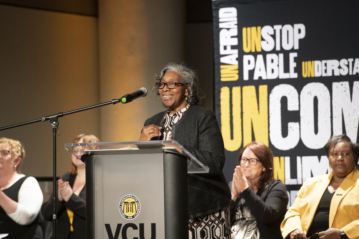 A woman speaking at a podium with four people seated behind her. 