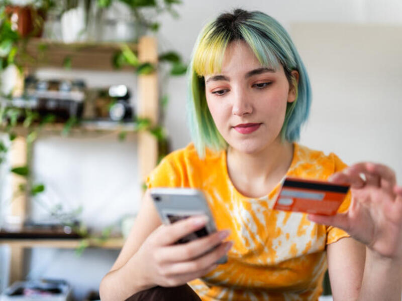 A photo of a person sitting and holding their phone and a credit card. 