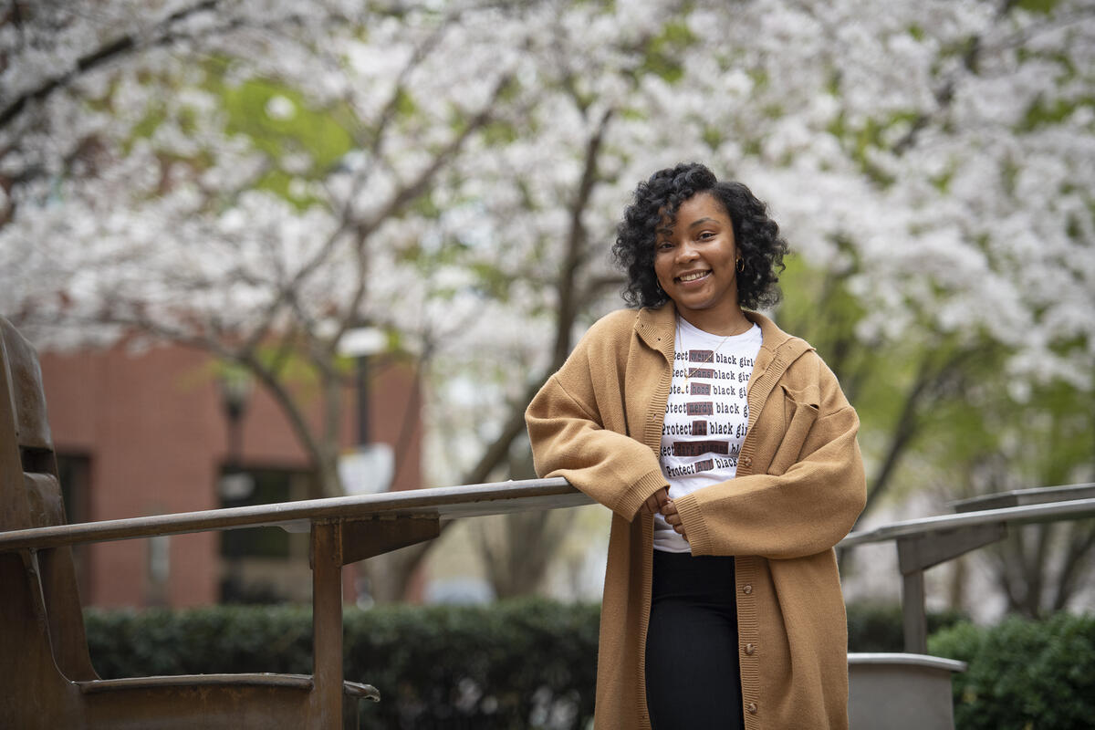 Akira Goden leaning on a hand railing in front of blooming cherry blossom trees