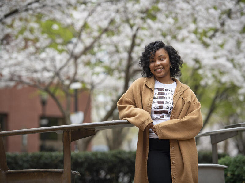 Akira Goden leaning on a hand railing in front of blooming cherry blossom trees