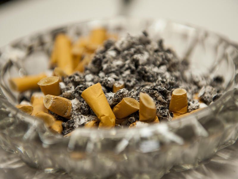 A glass ashtray filled with cigarette butts and ash
