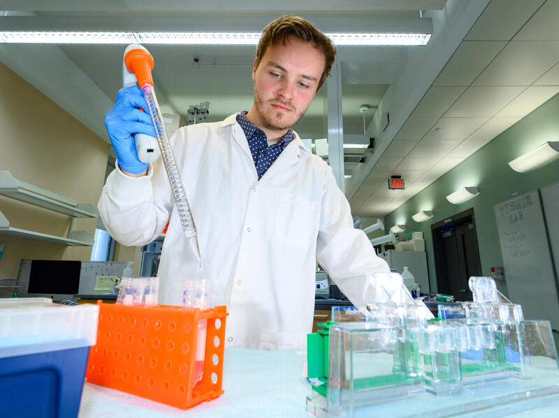 A photo of a man in a white lab coat standing in front of beakers