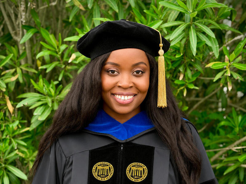 A woman smiling in graduation cap and gown attire.