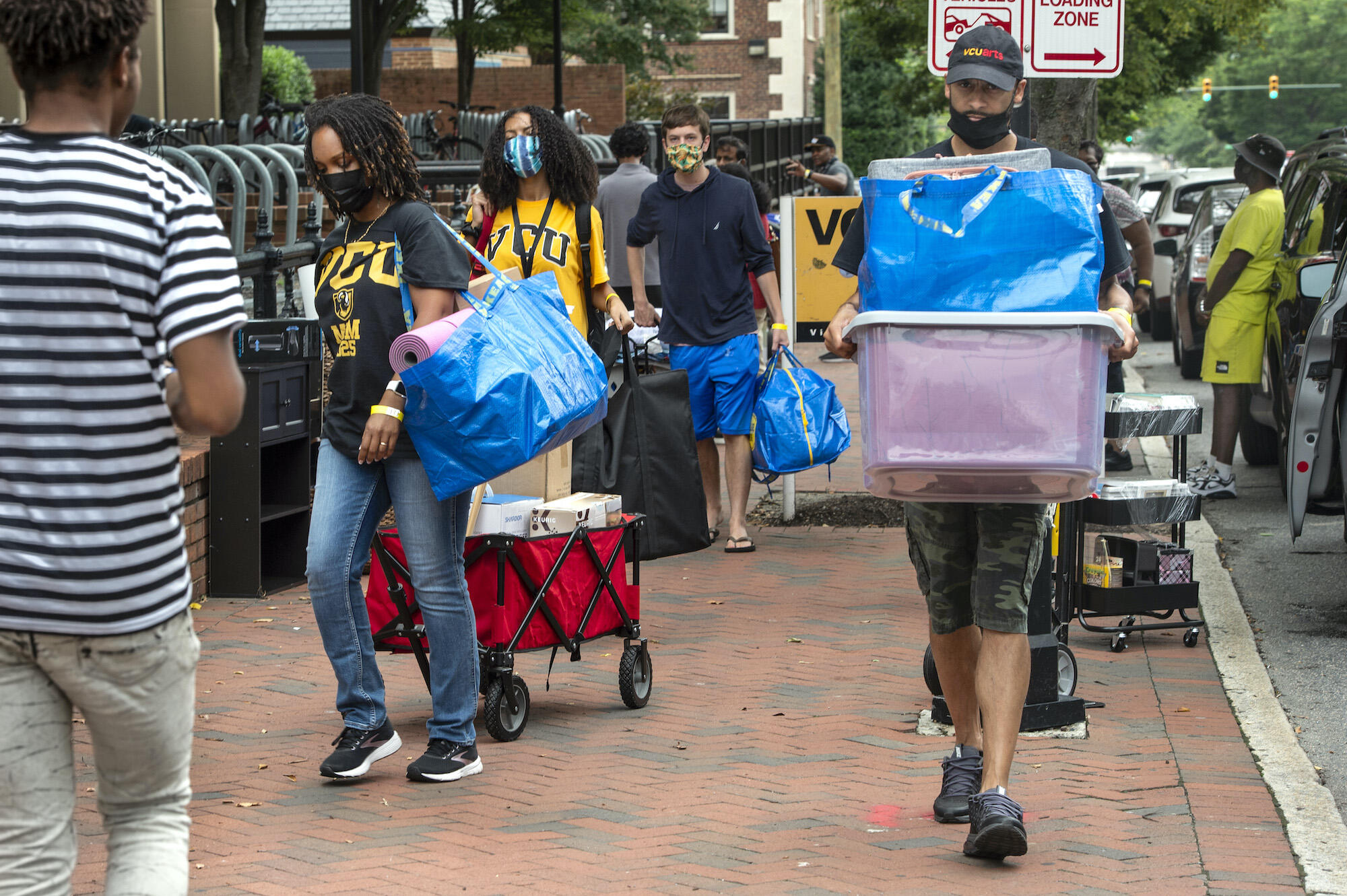 Students, with help from family and friends, haul and wheel boxes and bins along the sidewalk in front of Brandt and Rhodes halls. 