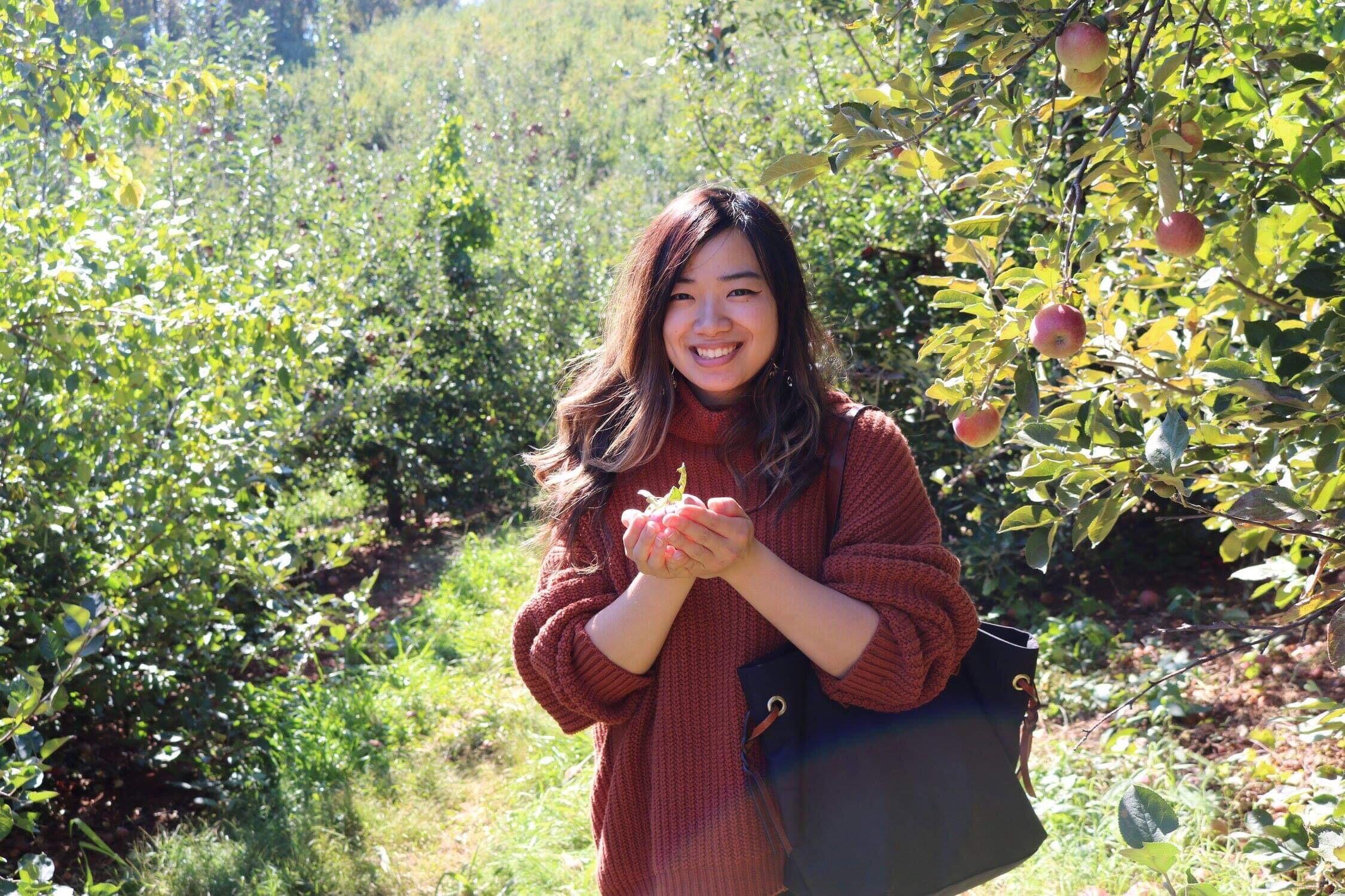 Student stands in garden with flower.