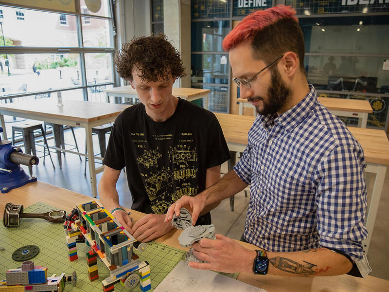 A student and a professor in a classroom work together building LEGOs.