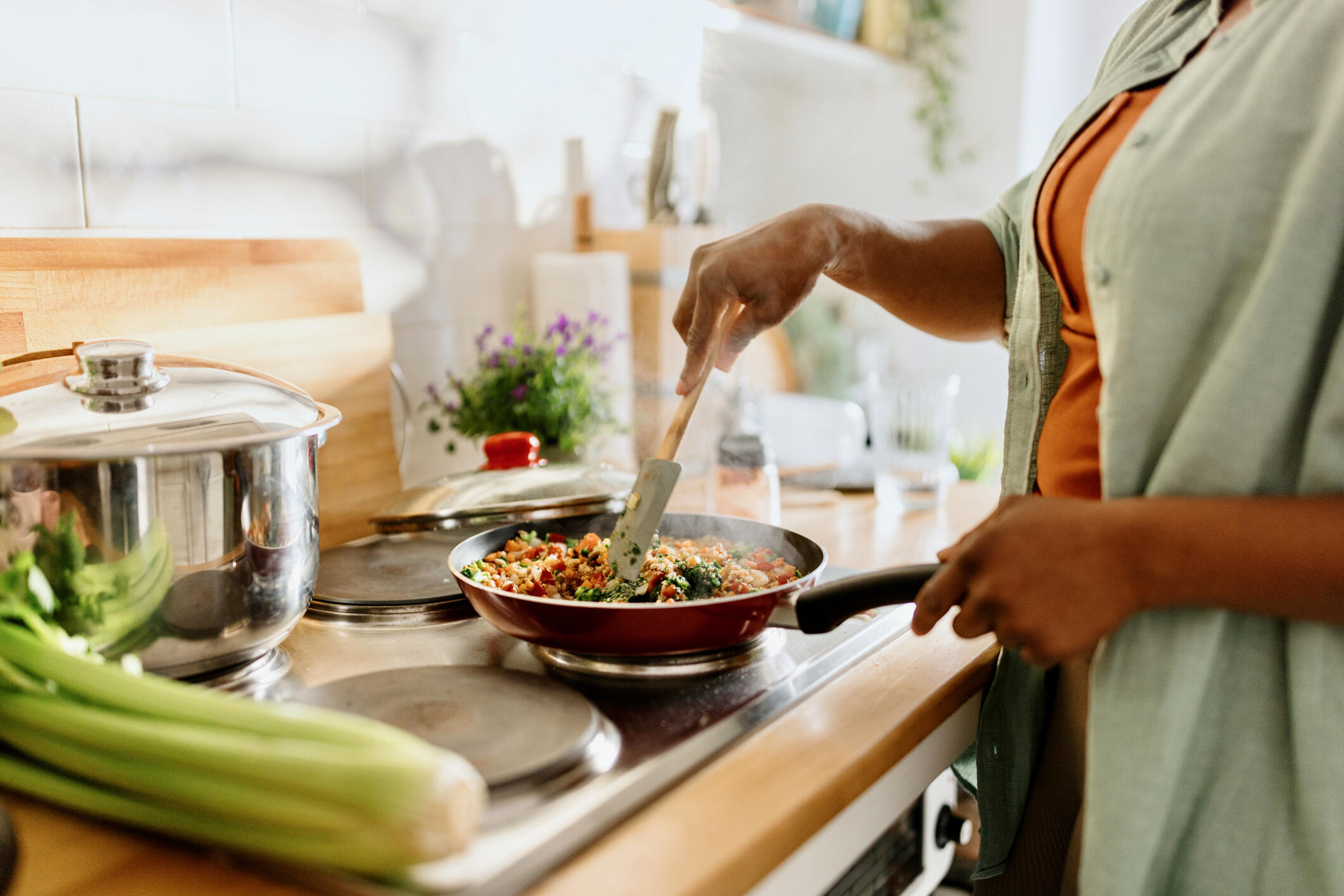 A photo of a woman from the neck down cooking food in a frying pan on a stove. 