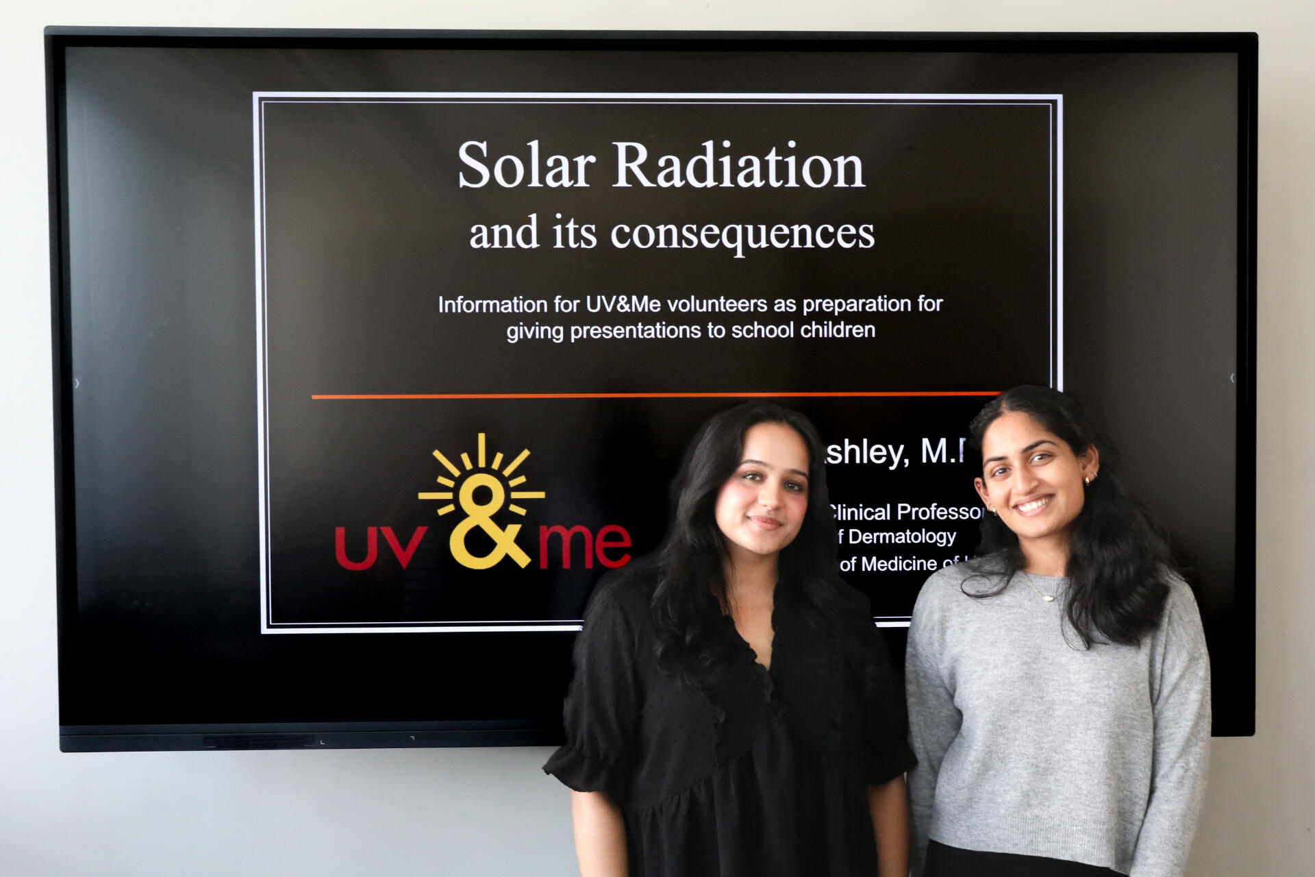 A photo of two women standing in front of a screen. The srcreen reads \"Solar Radiation and its consequences\" \"Information for UV&Me volunteers as preparation for giving presentations to school children.\" \"UV&me\"