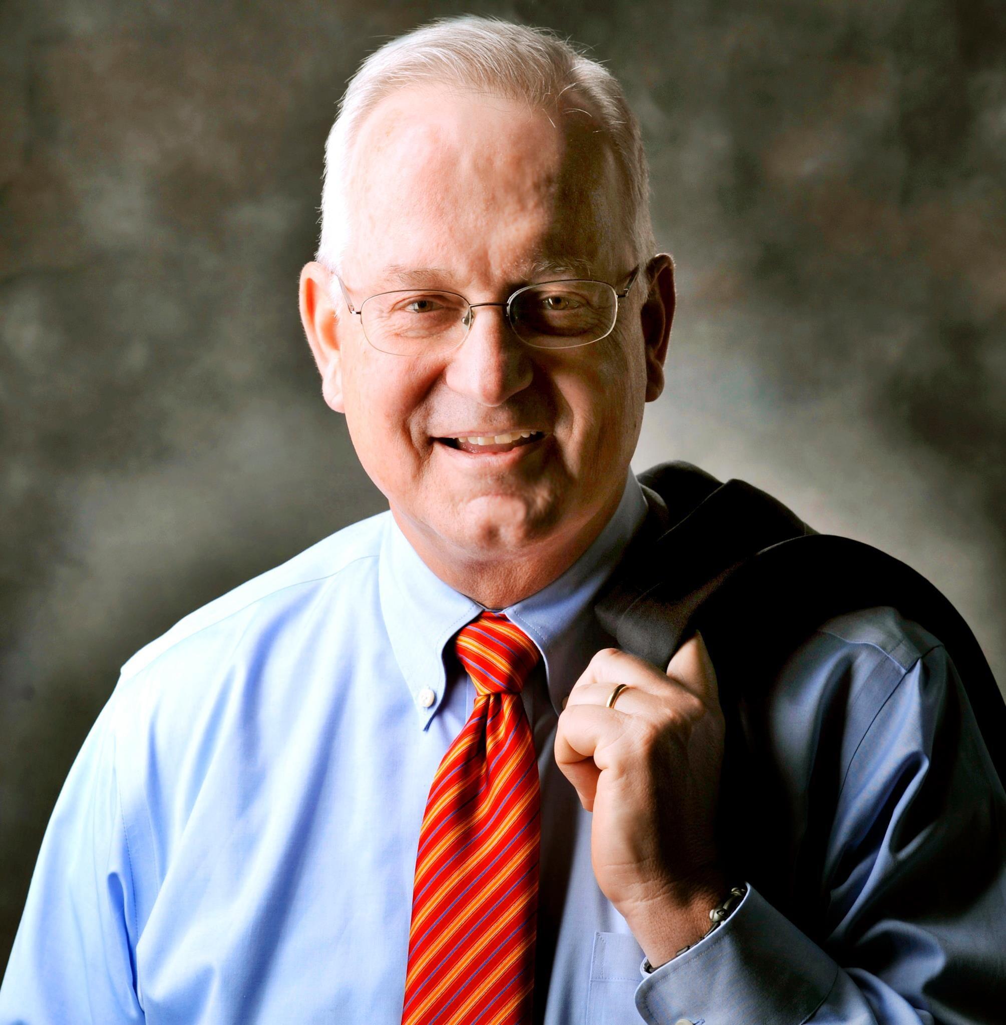 A photo of a man wearing a tie and a button-up shirt. He had draped his suit coat over his shoulder. 