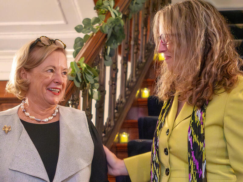 A photo of two women taking to each other in front of a stair case