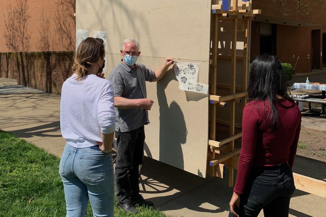 Students Stephanie Wilburn, left, and Nishta Chawla discuss their art work with associate professor Camden Whitehead.
