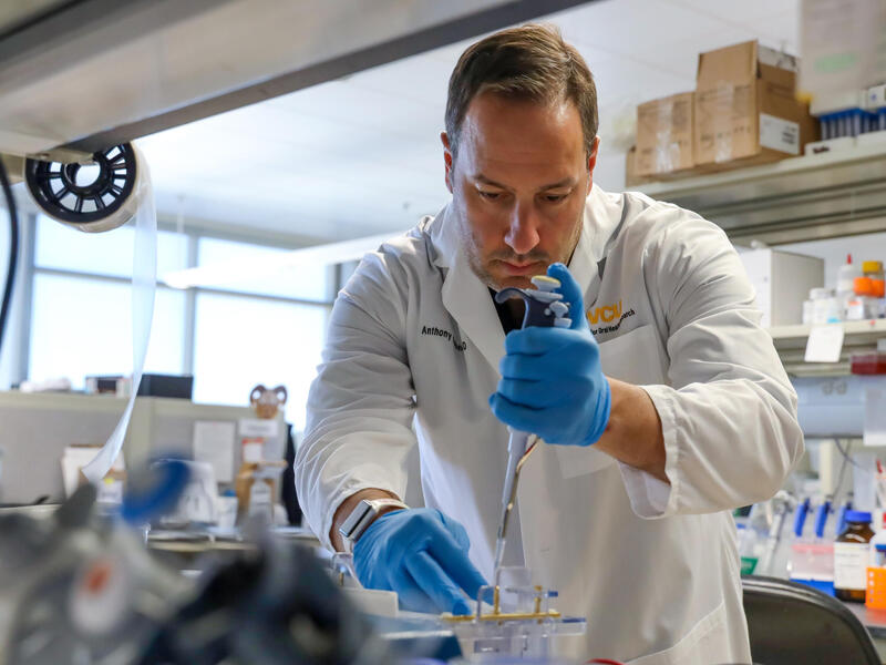 A photo of a man wearing a lab coat and latex gloves using scientific equipment 