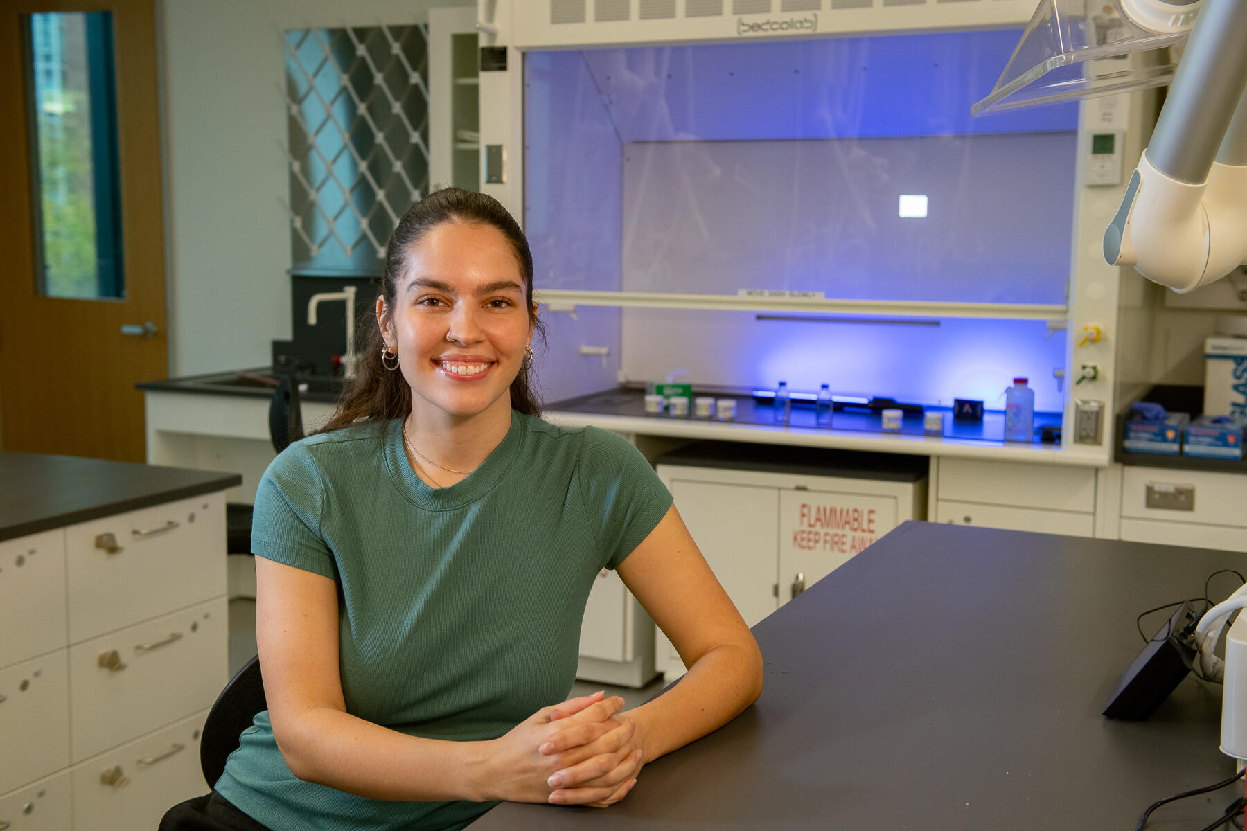 Woman in green shirt sits at a lab table.