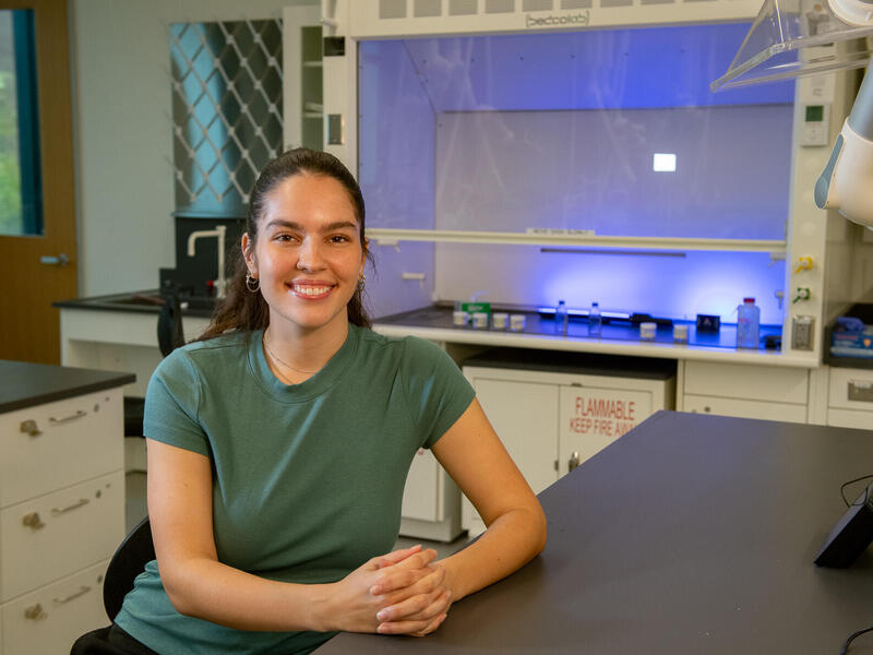 Woman in green shirt sits at a lab table.