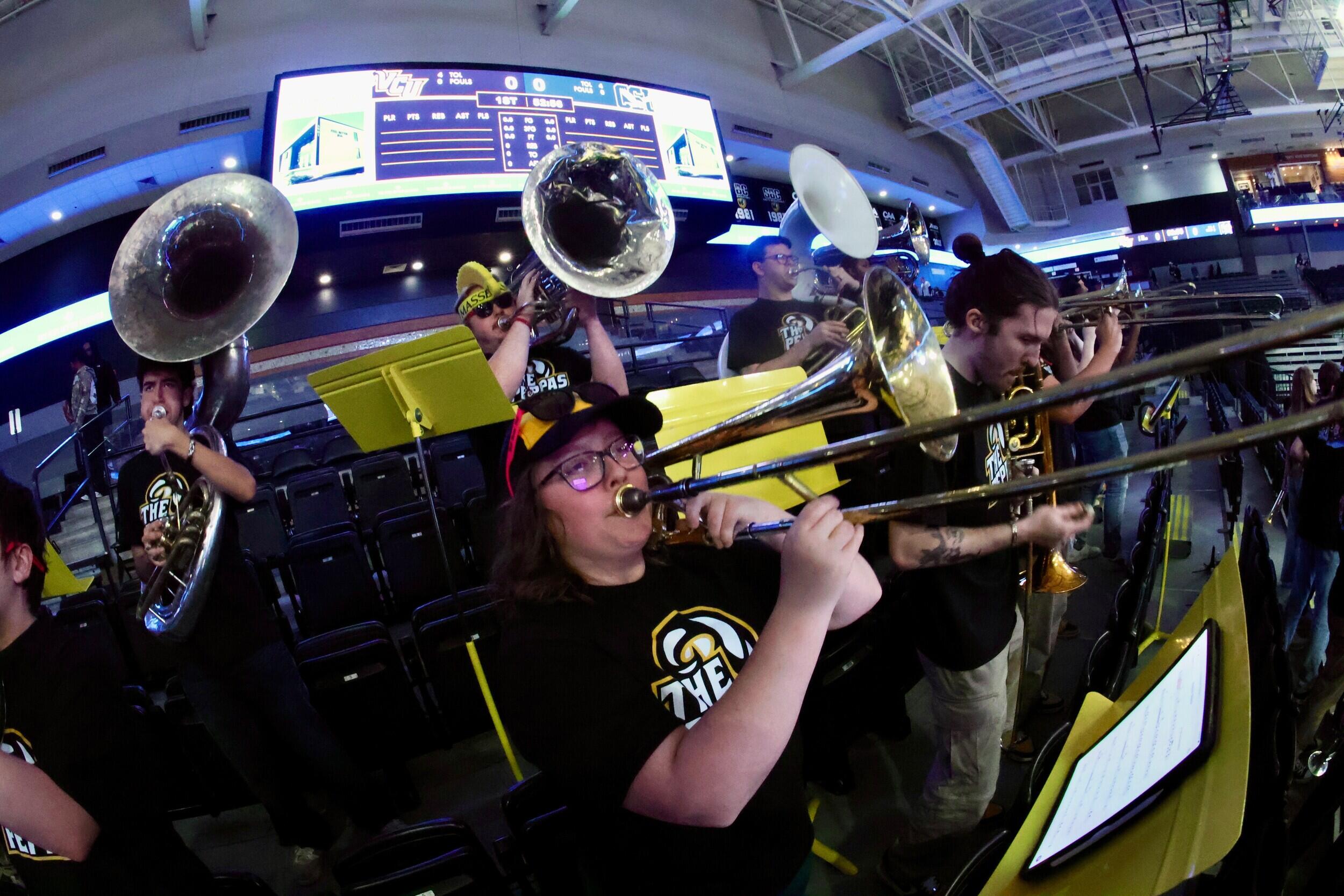 A photo of a a woman playing the trombone. Around her are other people playing wind instruments. 