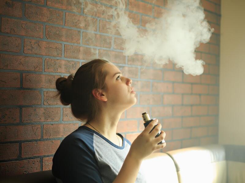 A user of an e-cigarette exhales vapor.