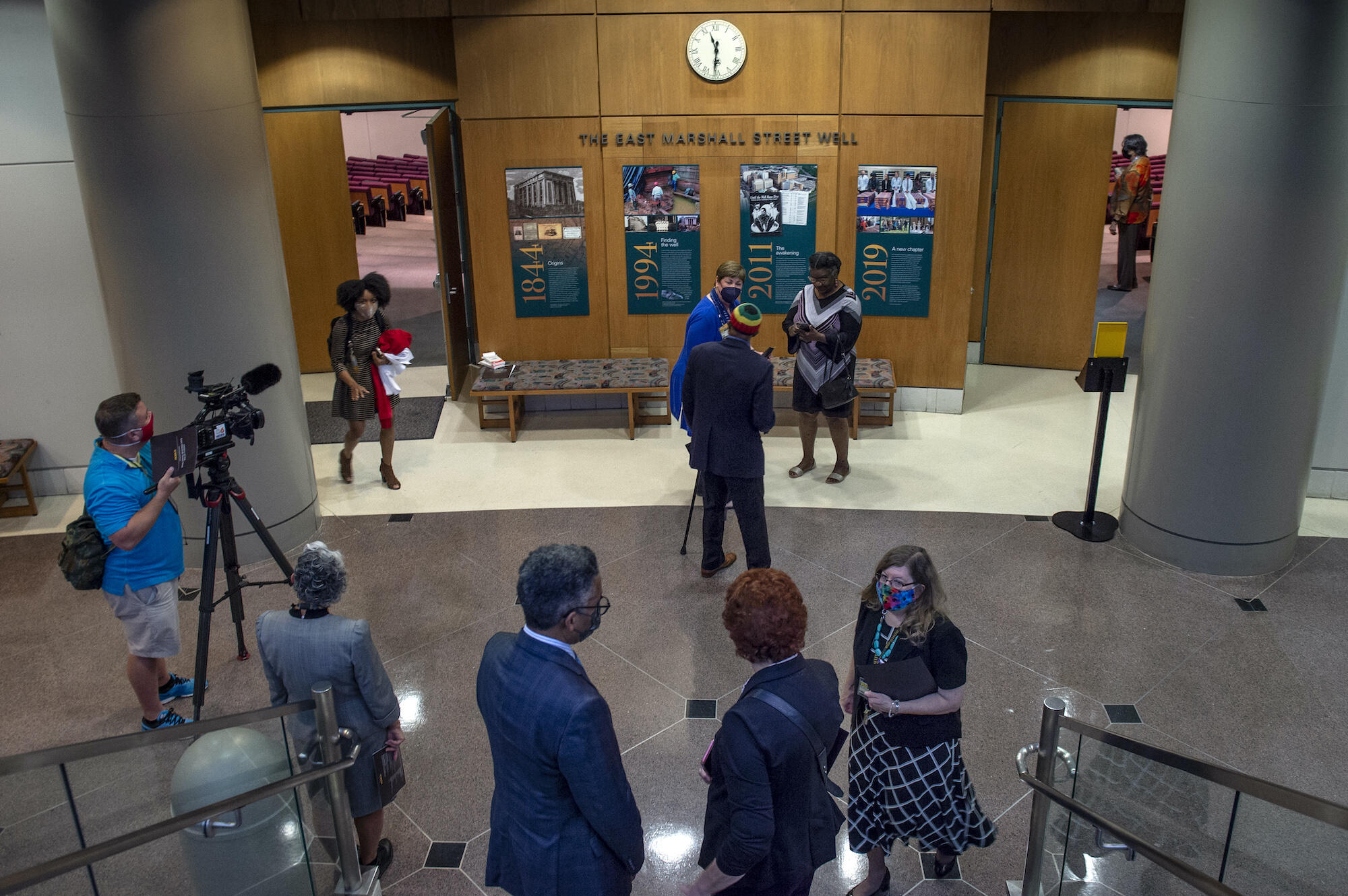 people gather in a lobby at VCU near a set of panels commemorating 19th-century human remains found in an MCV Campus well