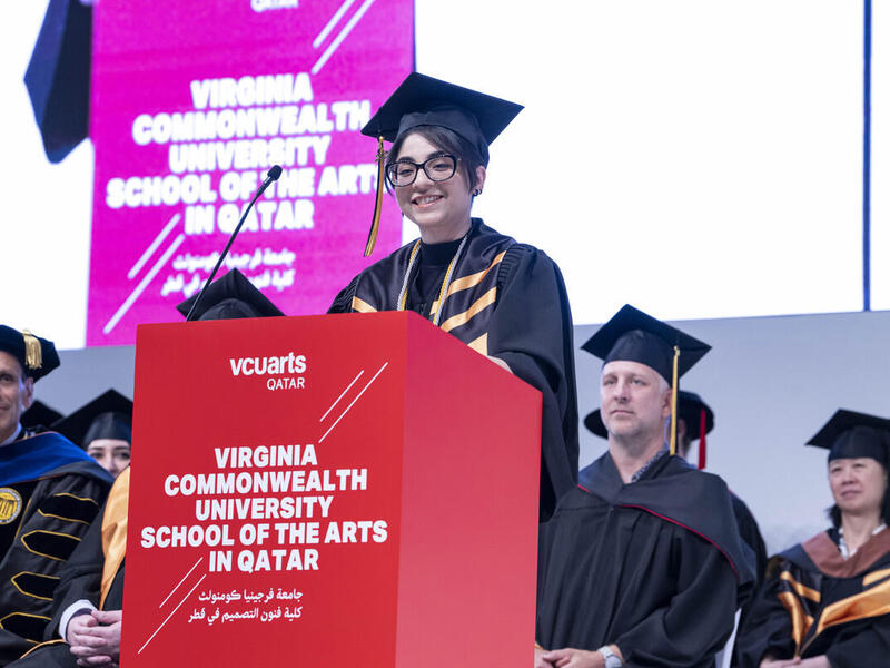 Fatima Nazir speaks at a lectern in graduation attire.