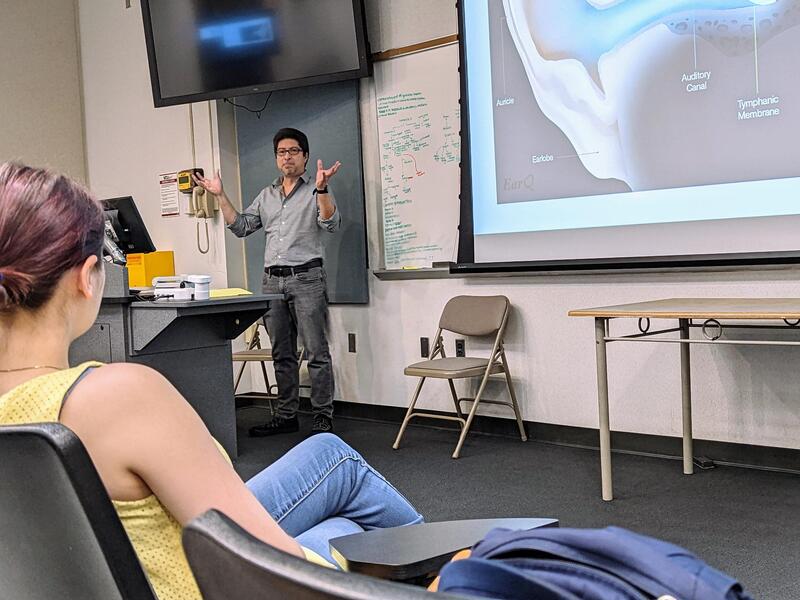 A man standing in the front of a classroom giving a lecture to students. 