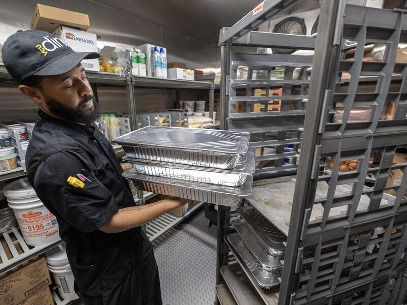 A photo of a man putting trays of food on a food cart