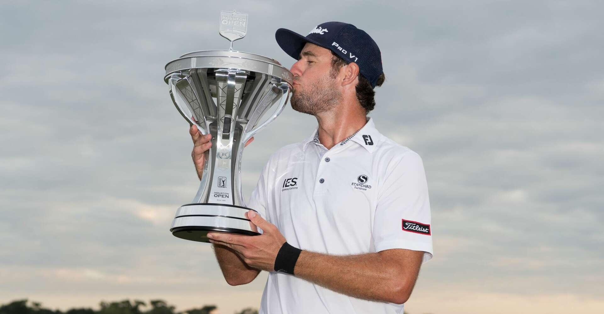 A photo of a man wearing a white polo shirt and baseball cap kissing a large silver trophy. 