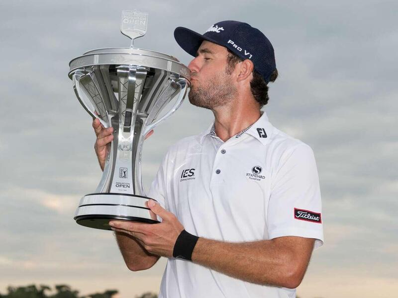 A photo of a man wearing a white polo shirt and baseball cap kissing a large silver trophy. 