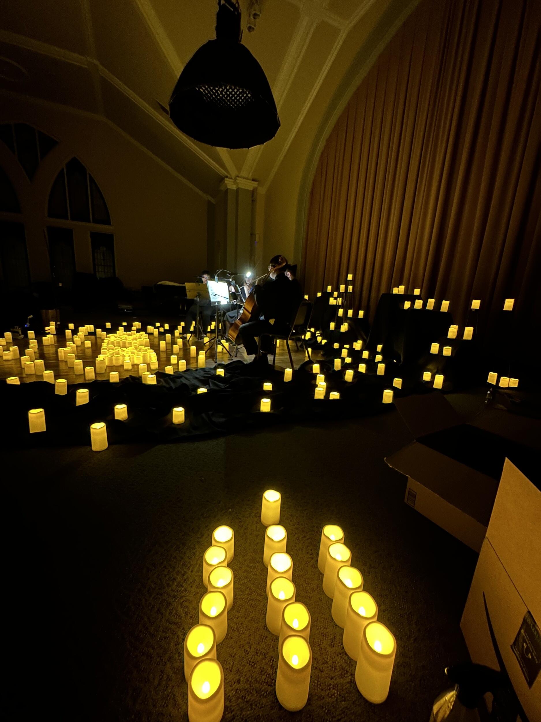 Hundreds of candles surround musicians on a dark stage.