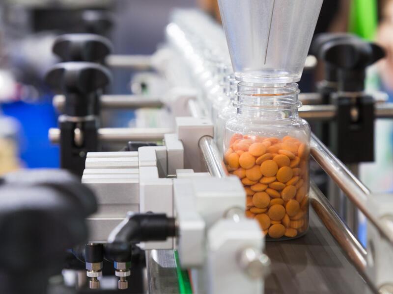 A manufacturing facility produces pharmaceutical products, including a bottle of orange pills, on a machine.