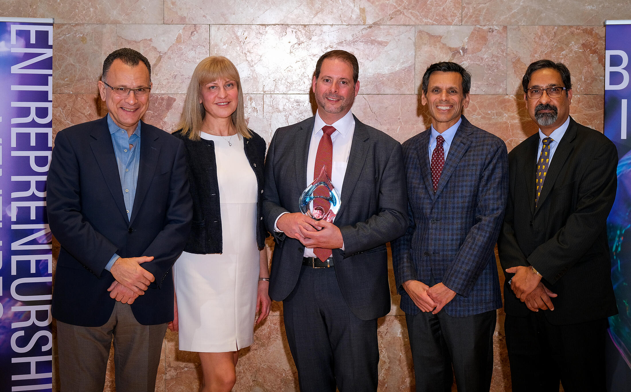 Five people standing next to each other. A man in the middle is holding a glass trophy.