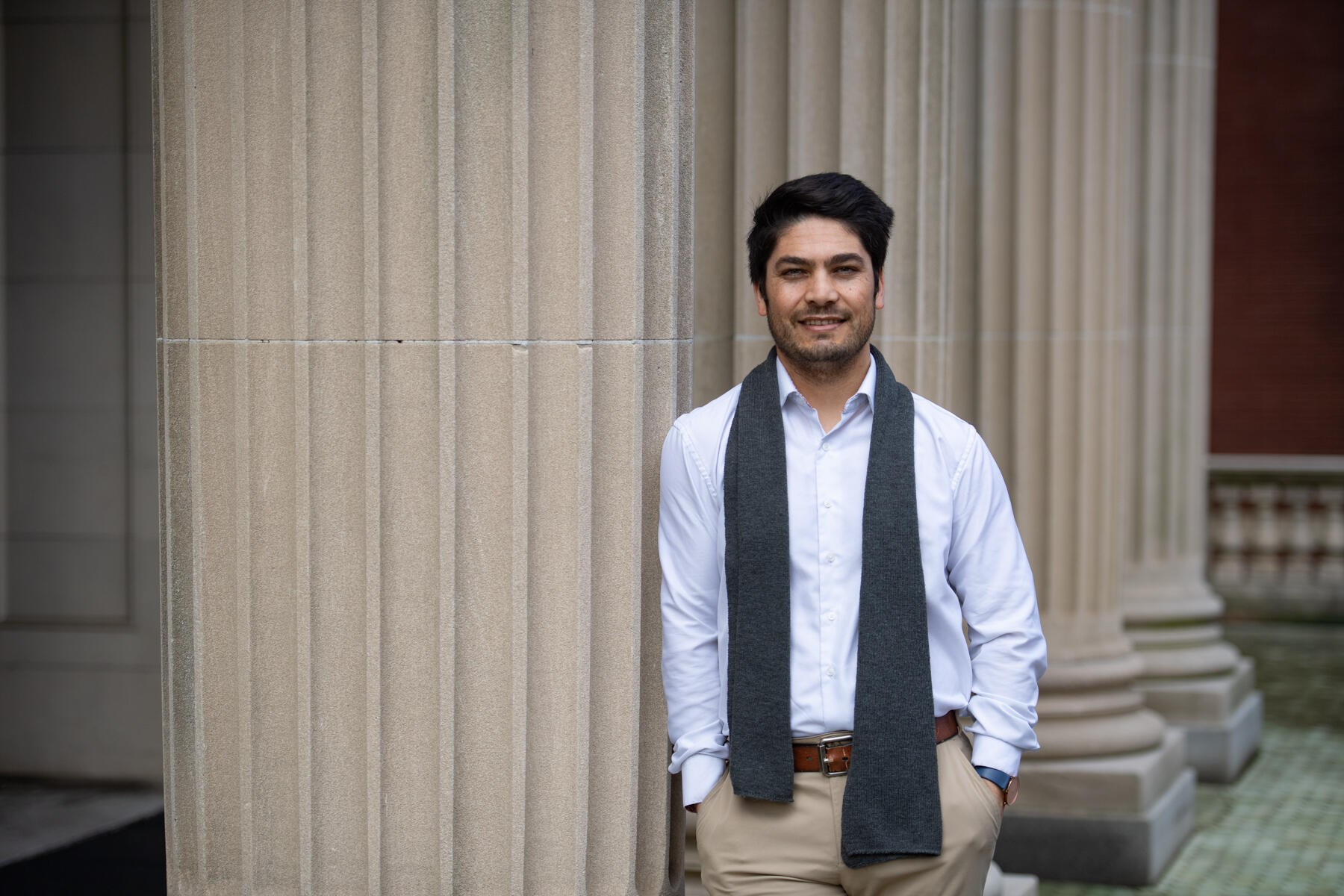 A photo of a man leaning against an ivory stone column. 