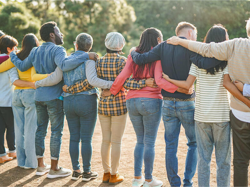 A photo of 10 people from behind. They are standing side by side with their arms wrapped around each other's backs. 
