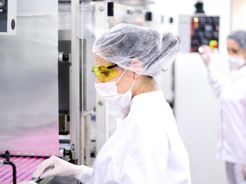 Student in lab with mask handles pink pills. 
