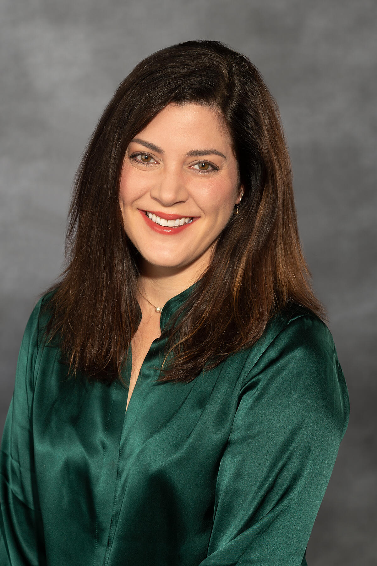 A portrait of a woman with brown hair wearing a dark green button up shirt. 