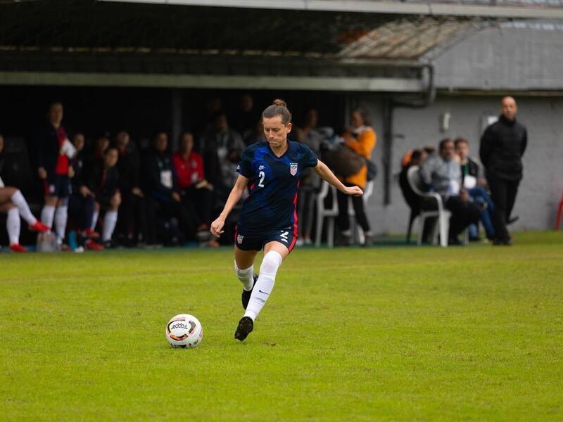 A woman on a soccer field running up to a ball to kick it 