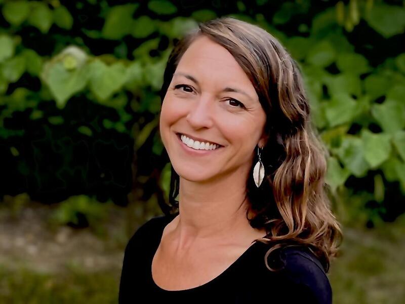 A wearing all black woman outside in front of foliage 