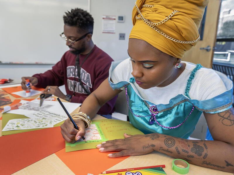 A photo of two people sitting at a table, writing on cards. 
