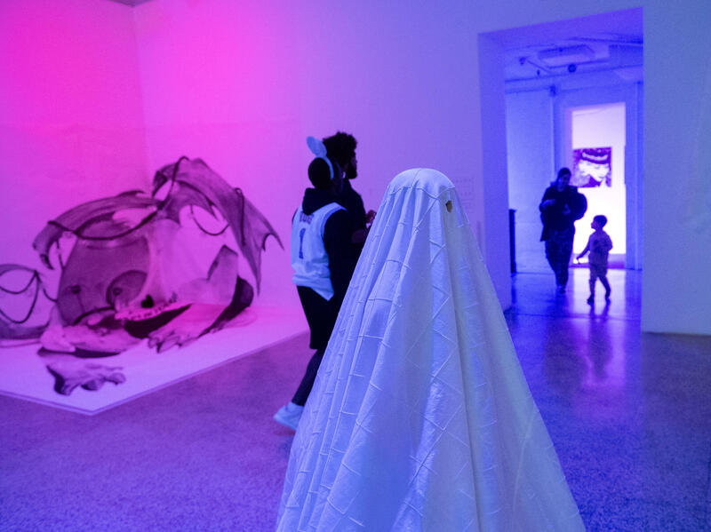 Someone dressed as a ghost in a white sheet stands in the middle of a room.