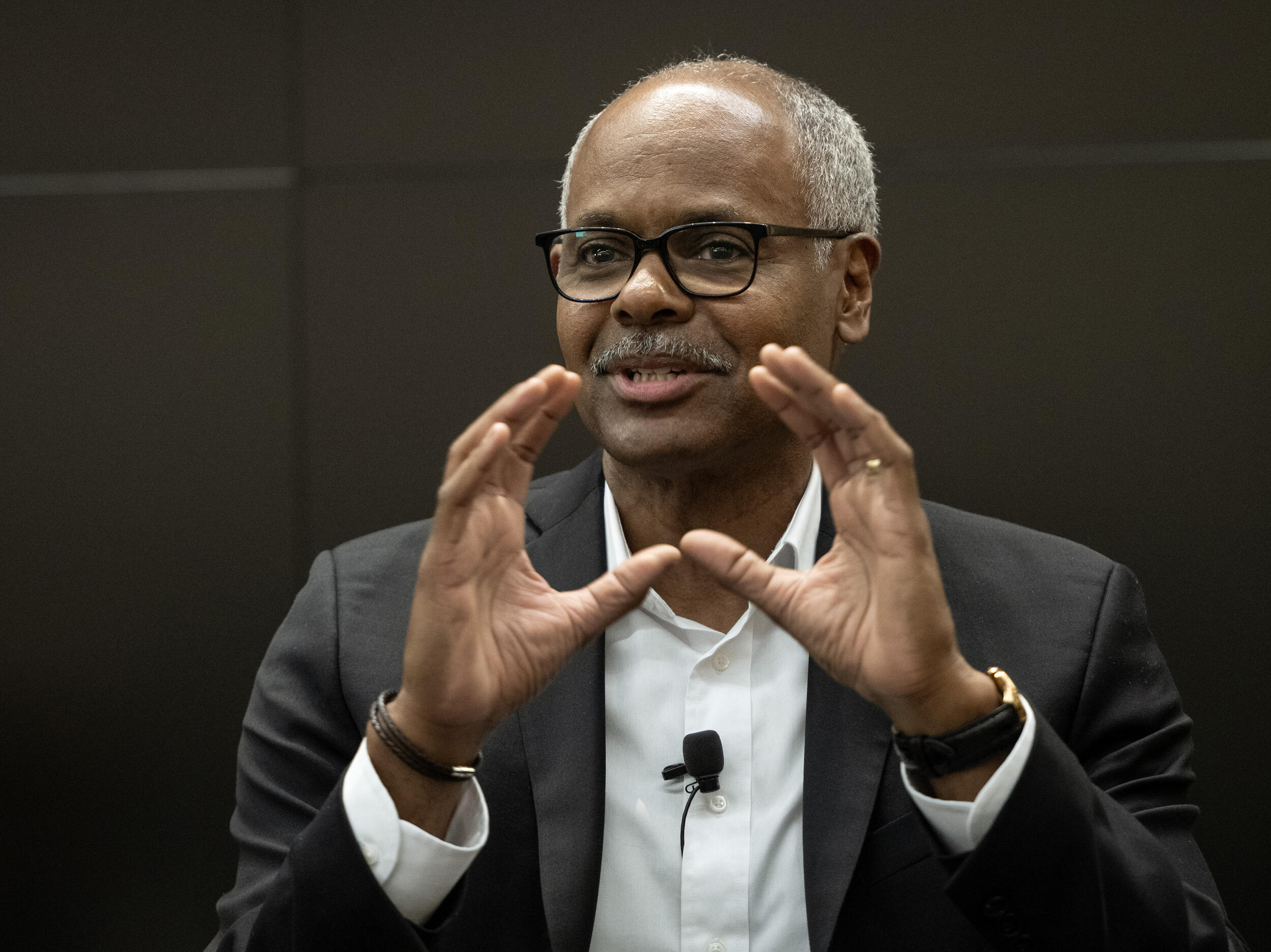A photo of a man speaking while gesturing his hands in front of him. 