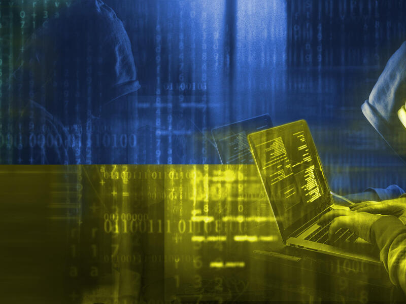 A graphic of a man wearing a hoodie typing on a laptop with an image of the Ukrainian flag in the background. 