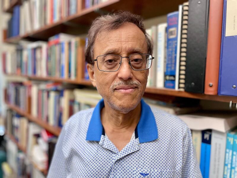 Head and shoulders portrait of Supriyo Bandyopadhyay standing in front of shelves of books.