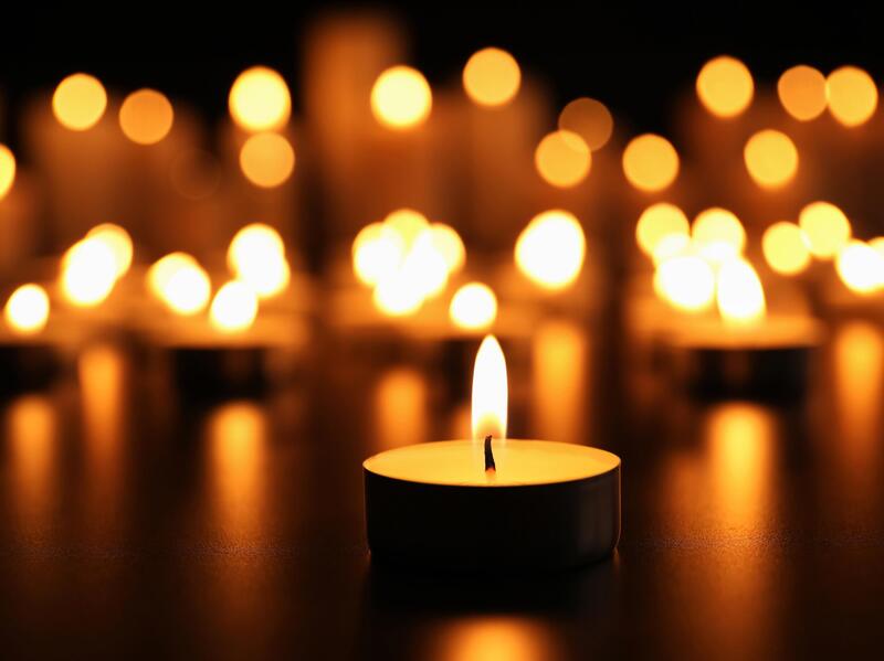 A tealight candle burning in a dark space with many others lit behind it. 