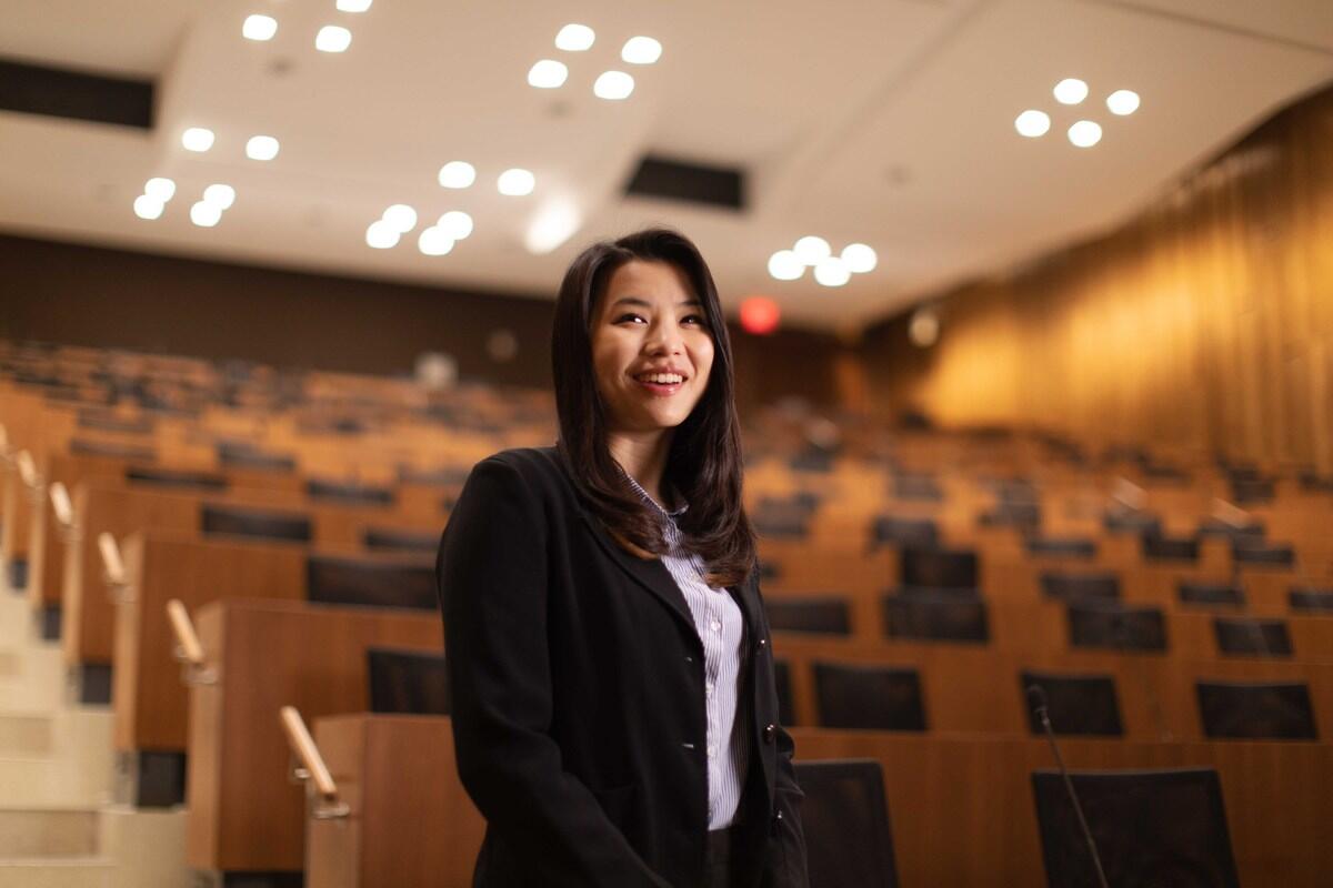 A woman wearing a black blazer standing in an lecture room in front of rows of chairs