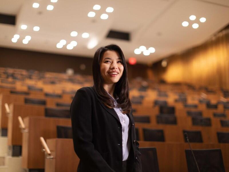 A woman wearing a black blazer standing in an lecture room in front of rows of chairs