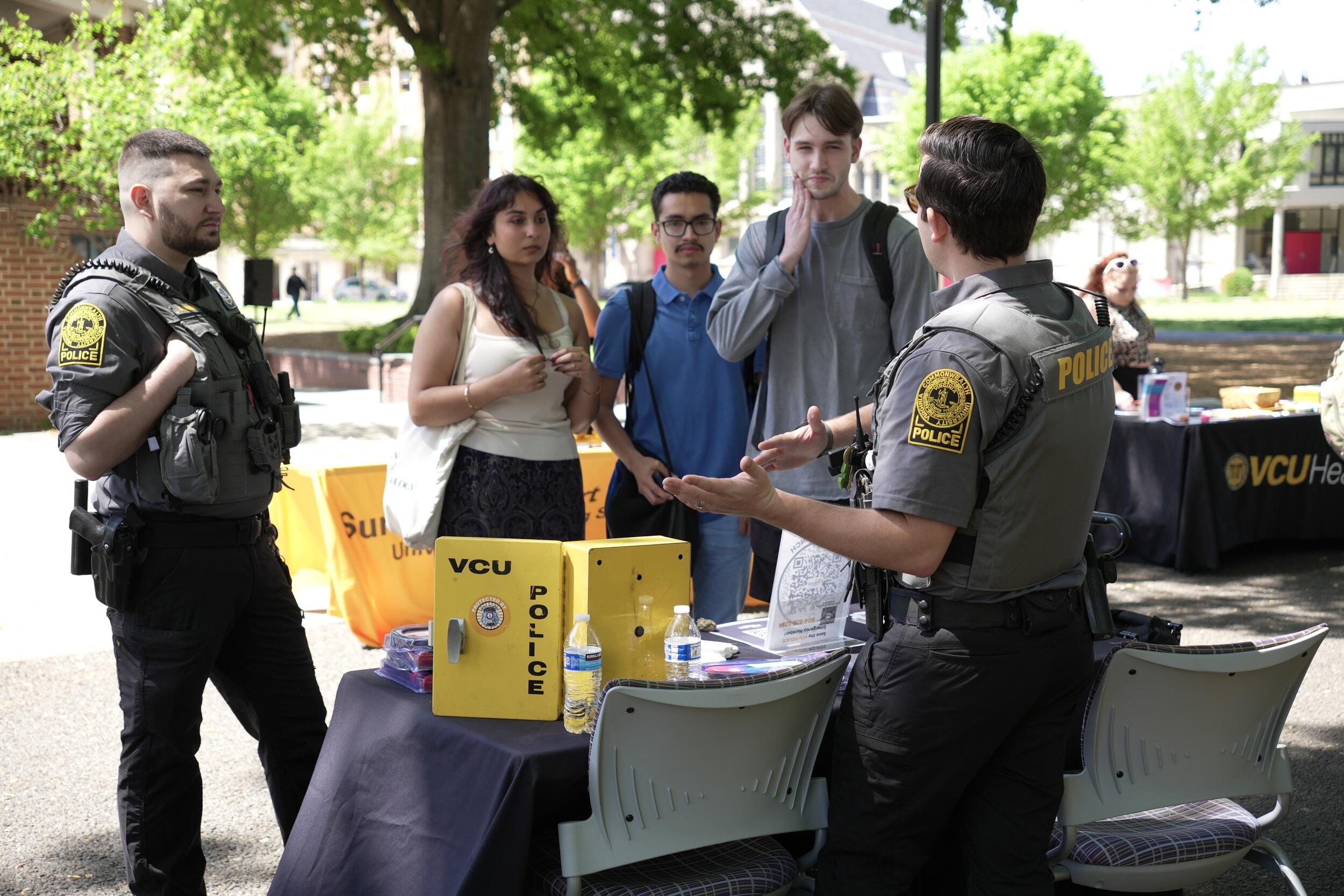 A photo of two police officers talking to three students. 