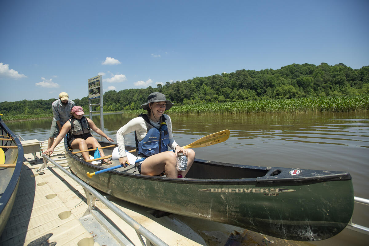 Two women sitting in a canoe with a man behind them bracing the boat 