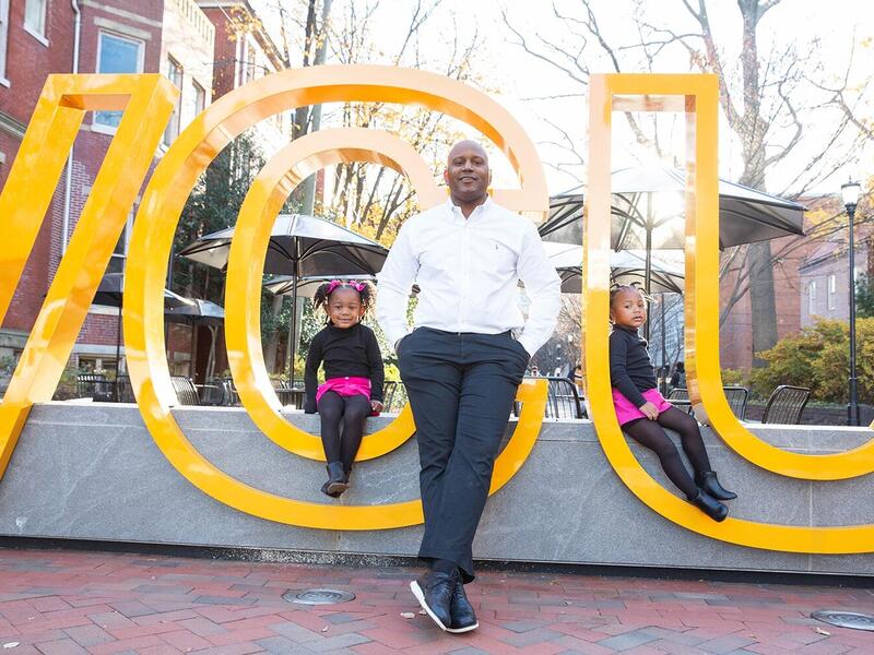 LeQuan Hylton sitting in the middle with daughters Carter (left) and Emory (right) on a VCU sign